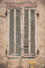 An old wooden window shutter with flaking white paint and rusting brackets on a crumbling old building at Girolata on the Mediterranean island of Corsica
