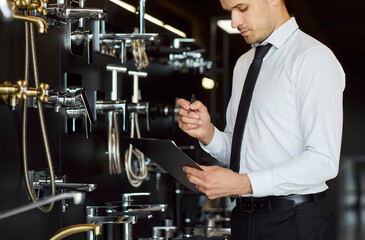Male consultant conducts inventory of taps and faucets in a plumbing store. Specializing in hardware for bathroom and kitchen, he ensures all water related products are accounted for.