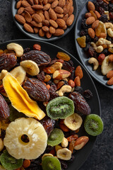Dried tropical fruits, nuts, and raisins in black plate.