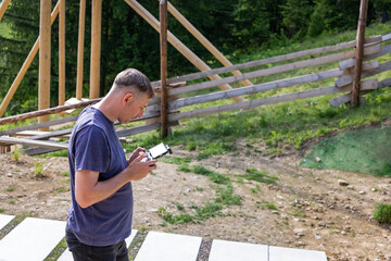 Man operating drone outdoors in rural area. Adult man standing on a path with a drone controller,...