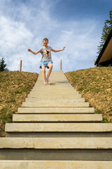 Young girl joyfully running down outdoor steps. Smiling girl in casual clothes runs barefoot down...