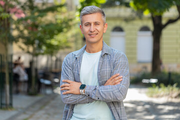 Portrait of happy mature man smiling friendly, while standing arms crossed, glad expression looking...