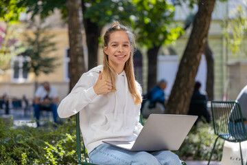 Happy young woman girl using laptop sitting on chair in urban city street outdoors. Caucasian girl...