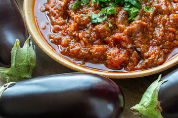 Zaalouk - Moroccan eggplant and tomato dip in a bowl, fresh eggplants in the foreground. Selective focus.