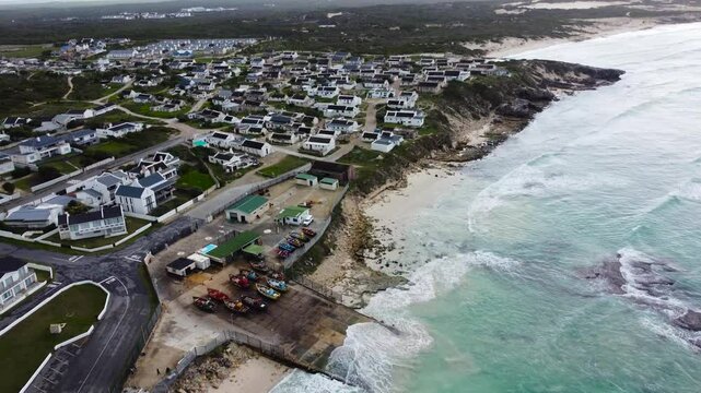 Camera panning up along the coastline and the town of Waenhuiskrans Arniston,, a coastal town, 4K Aerial Video