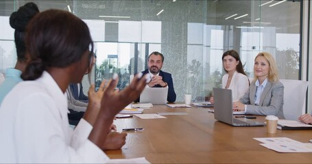 Group of confident young business people listening to female african american colleague discussing new startup sitting at desk on meeting. Company employees talking in office. 4k video. - Powered by Adobe