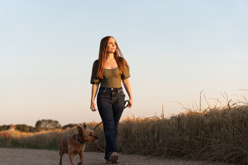 Young woman with her dog walking at sunset in the countryside