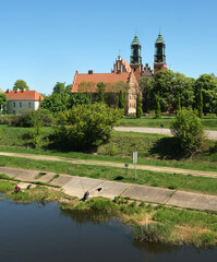 Historic twin-towered Basilica of St. Peter and Paul rises amid greenery on Ostrow Tumski, under a clear blue sky in Poznan, Poland.