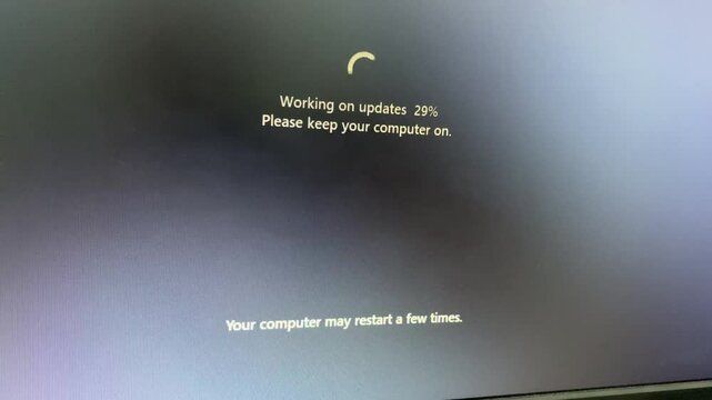 A computer screen displays a message indicating that the operating system is "Working on updates 29%," advising the user to keep the computer on and noting that it may restart multiple times.