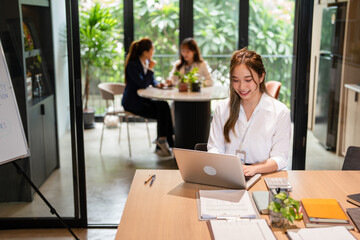 Young asian businesswoman using laptop for remote work .young woman sits at office desk , texting,...