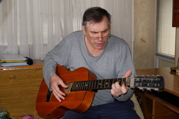 Obraz premium Man at home playing an old guitar, hands are visible, instrument, postures of a person, hand on the neck of an object