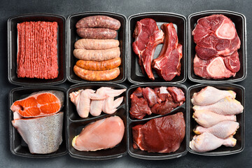 Black plastic packaging trays from supermarket with different types of fresh raw meat cuts, fresh beefbeef steaks, fish and variety meats in boxes from above