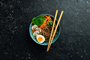 A bowl of Japanese noodles with mushrooms, carrots, onions and egg. On a stone background. Top view.