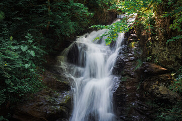 Obraz premium A waterfall cascades gracefully, creating a soothing sound as crystal-clear water tumbles over rocks into a serene pool below.