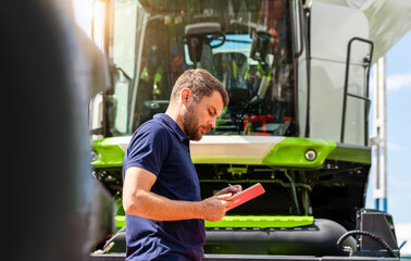 Male agricultural professional using tablet near combine harvester at agricultural machinery...