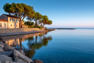 Fototapeta premium Calm mediterranean sea reflecting maritime pines and houses at sunrise