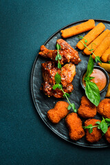 Beer snack plate: chicken nuggets, chicken wings, cheese and fries. On a dark background, close-up.