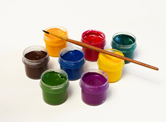 Seven jars with paints of different colors, a brush for painting lies on top of the jars, on a...
