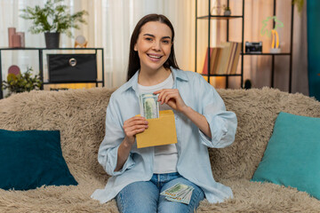 Young woman at home counting cash dollar bills, smiling satisfied while placing money into...
