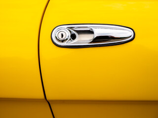 Close-up of a classic chrome car door handle on a bright yellow vintage vehicle. Minimalist...