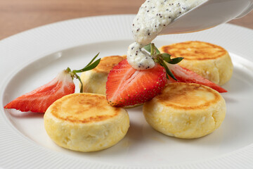 Cottage cheese pancakes or syrniki decorated with fresh strawberries and poppy seed sauce on white plate