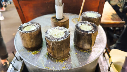 Traditional Indonesian street food cooked in a bamboo mold over a hot steamer (kue putu), commonly used to make kue putu or similar steamed rice cakes.