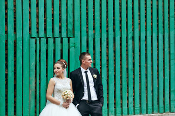 A bride and groom stand in front of a green wall