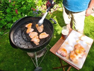 Man enjoying a sunny day while putting chicken thighs on his backyard grill