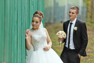 A bride and groom are standing in front of a green fence