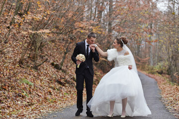 A bride and groom are walking down a road, the bride is wearing a white dress