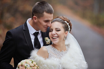 A bride and groom are posing for a picture, the bride is wearing a white dress