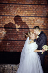 A bride and groom are kissing in front of a brick wall