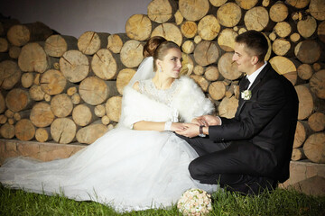 A bride and groom are sitting on the grass, holding hands