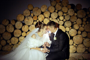 A bride and groom are sitting together in front of a pile of logs