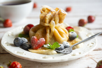 Delicate pancakes with fruits and berries on a wooden table.
