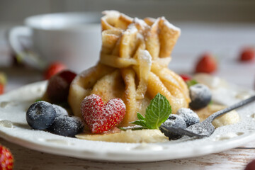 Delicate pancakes with fruits and berries on a wooden table.