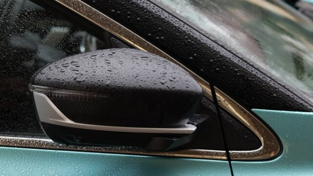 The car has a black and silver mirror. The mirror is wet. The car is green