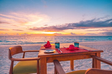 Romantic beach dinner setup with simple chairs and table facing the sea under a colorful sky with soft clouds, peaceful seaside atmosphere ideal for summer travel and oceanfront dining scenes
