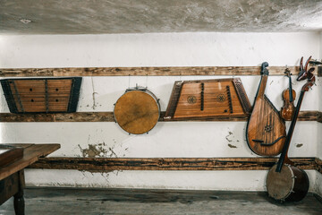 Row of traditional folk instruments—dulcimer, drum, bandura, violin, bass—neatly hanging on...