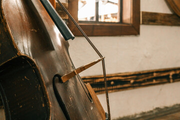 Close-up of weathered double bass with bow resting inside rustic folk house, showing scratched wooden surface, rich patina and traditional musical craftsmanship