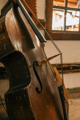 Close-up of weathered double bass with bow resting inside rustic folk house, showing scratched...