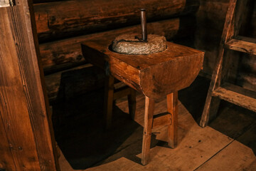 Rustic log-cabin interior with sturdy wooden chopping block supporting stone hand mill,...