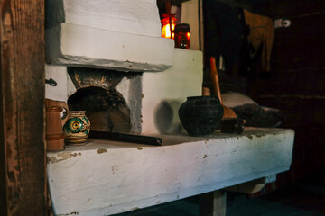 Traditional white clay hearth in a rustic cabin kitchen, glowing kerosene lantern, pottery and wooden utensils evoke a cozy sense of folk heritage