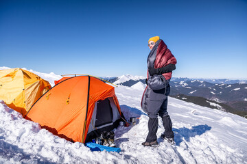 Smiling man wrapped in sleeping bag on snowy mountain near tent, enjoying morning outdoors
