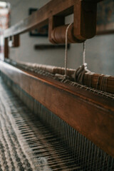 Traditional wooden loom with wool fabric in progress inside rustic folk house. Natural light enters...