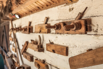 Oblique view of assorted antique wooden hand planes mounted on weathered white barn wall, showing rich patina, threaded clamp screws and rustic roof detail in traditional carpentry workshop