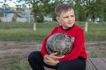 Adorable caucasian boy smiling happy holding soccer ball sitting in the park