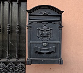 Typical Postbox in Spain. Featuring classic decorative relief and vintage design. Close-up of an old-fashioned postbox mounted beside an ornate wrought-iron window grille.