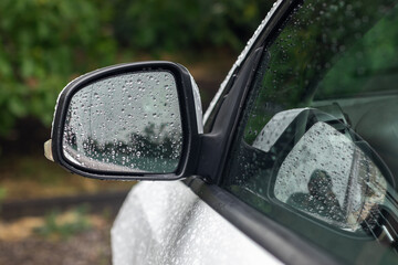 A car's rear view mirror is covered in raindrops