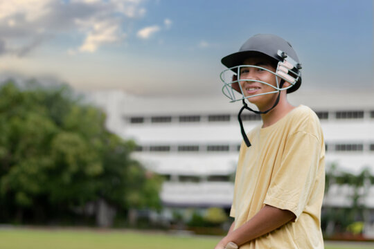 Young boy wearing a helmet holding cricket bat while playing cricket on a grassy field, focusing intensely as he hits the ball with a wooden bat. Outdoor sports and youth energy captured in motion. - Powered by Adobe